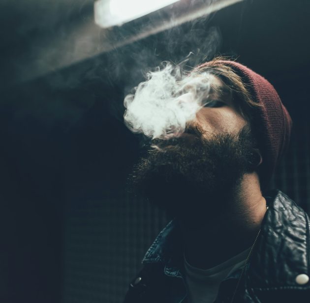 Young male hipster in knit hat smoking at night